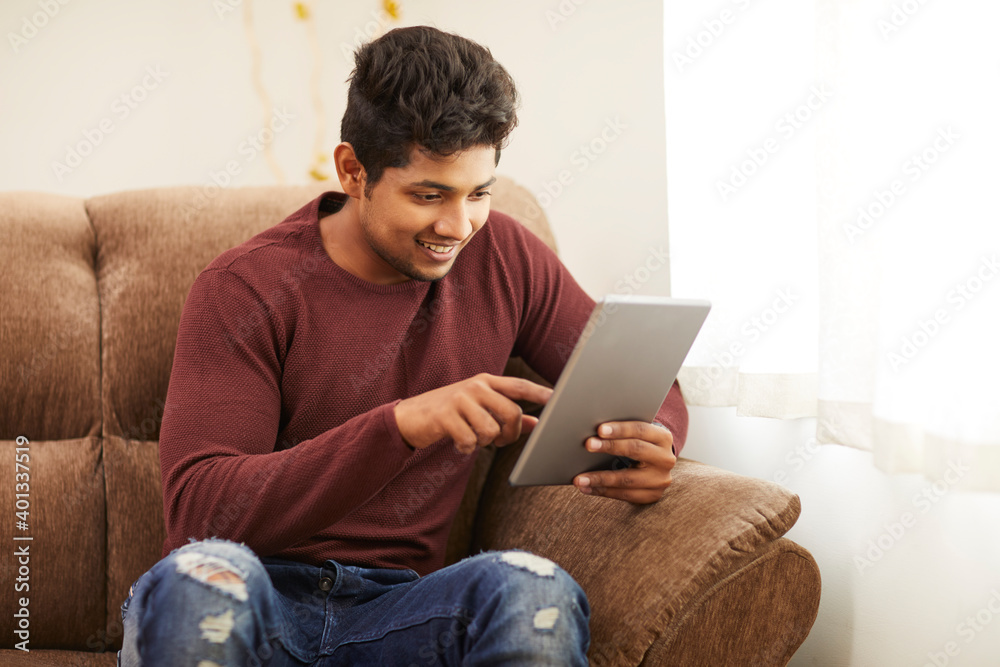 Handsome smiling young man using digital tablet on sofa at home. Handsome smiling young man using digital tablet on sofa at home.