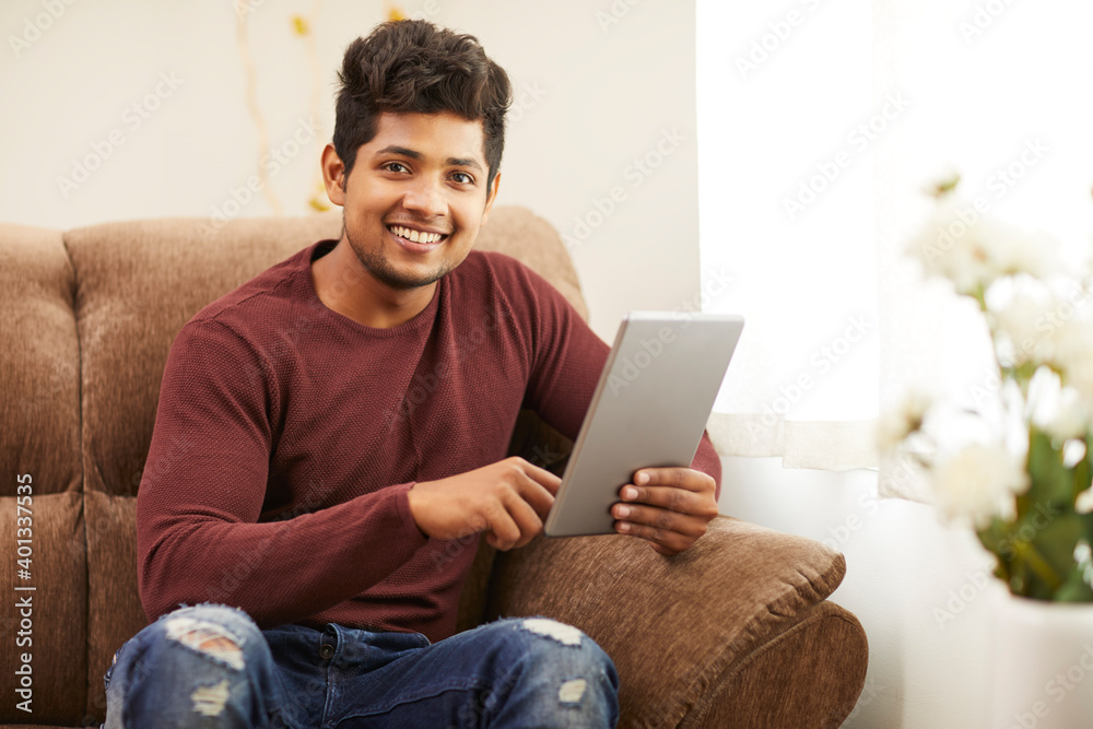 Handsome smiling young man using digital tablet on sofa at home. Handsome smiling young man using digital tablet on sofa at home.