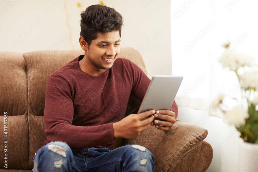 Handsome smiling young man using digital tablet on sofa at home. Handsome smiling young man using digital tablet on sofa at home.