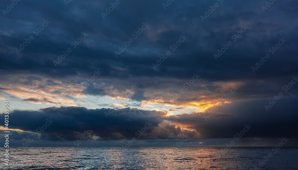 Dramatic evening sky over the sea. In the gap between dense storm clouds, orange illumination from the sun's rays. Reflection on a shiny water surface. Black Sea