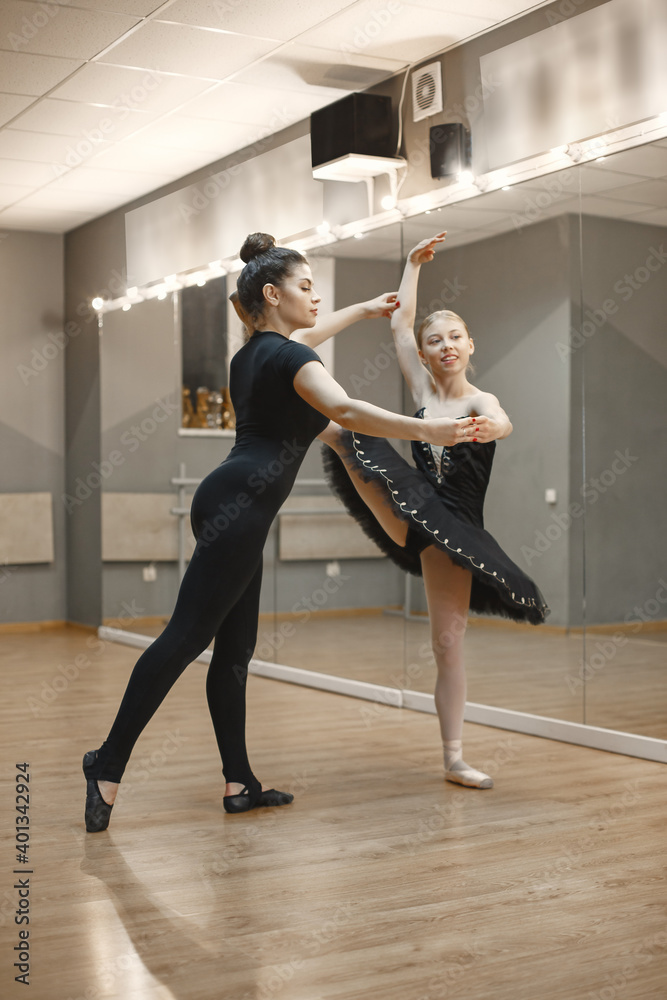 Obraz premium Cute little ballerina in black ballet costume. Young lady is dancing in the room. Girl in dance class with teatcher.