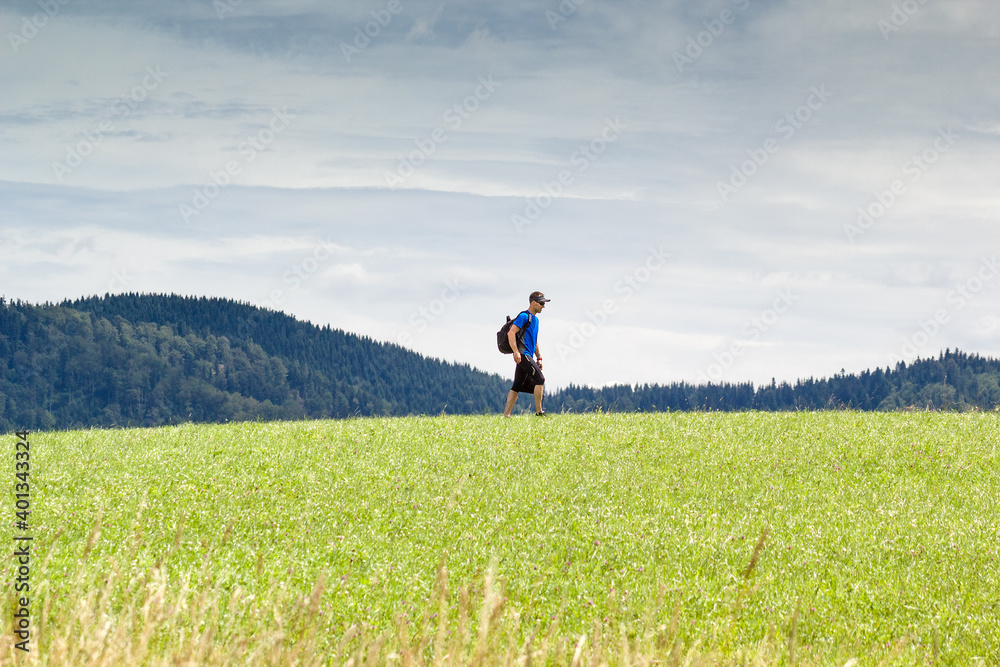 Man runner walking after training through fields at mountains background and carrying backpack and bag. Man runner walking after training through fields at mountains background and carrying backpack and bag.