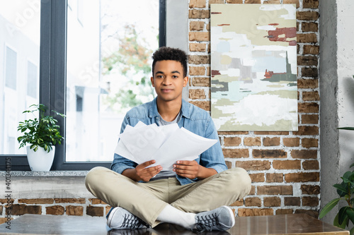 african american man sitting with crossed legs on desk and holding documents.