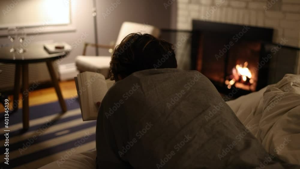 Person relaxing on the bed, reading a book in front of the fire. Person relaxing on the bed, reading a book in front of the fire.