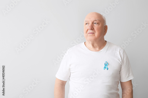 Senior man with blue ribbon on light background. Prostate cancer awareness co...