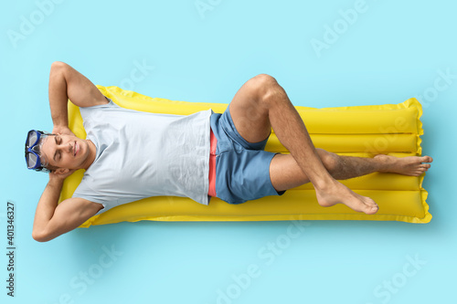 Young man lying on inflatable mattress against color background