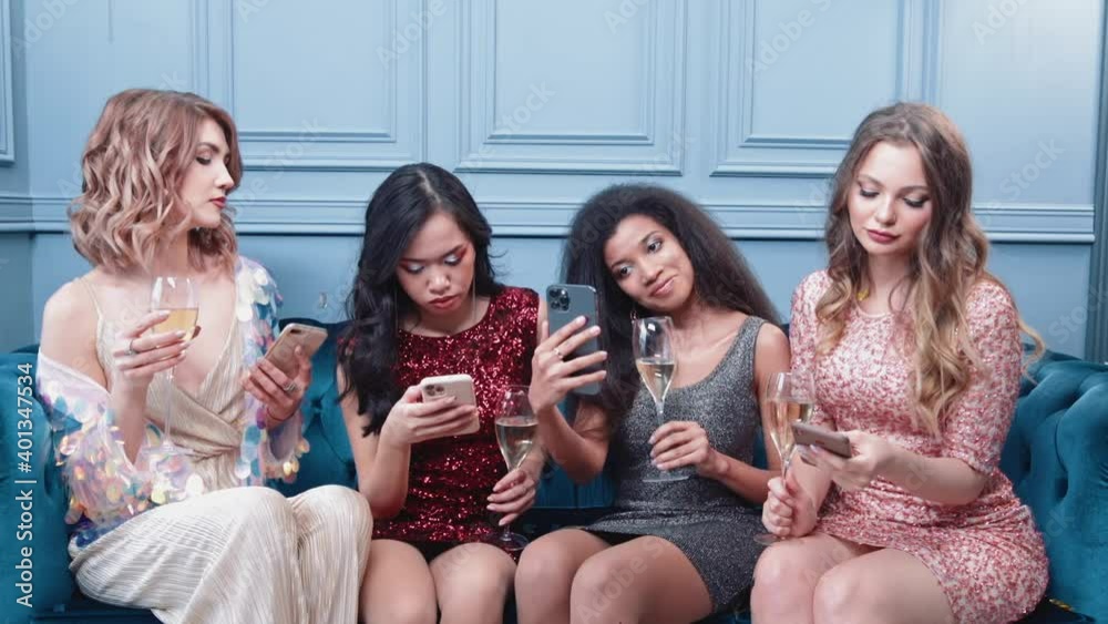 Glamorous females sitting in the lounge area in night club, use their smartphones and hold champagne glasses in their hands, online communication.