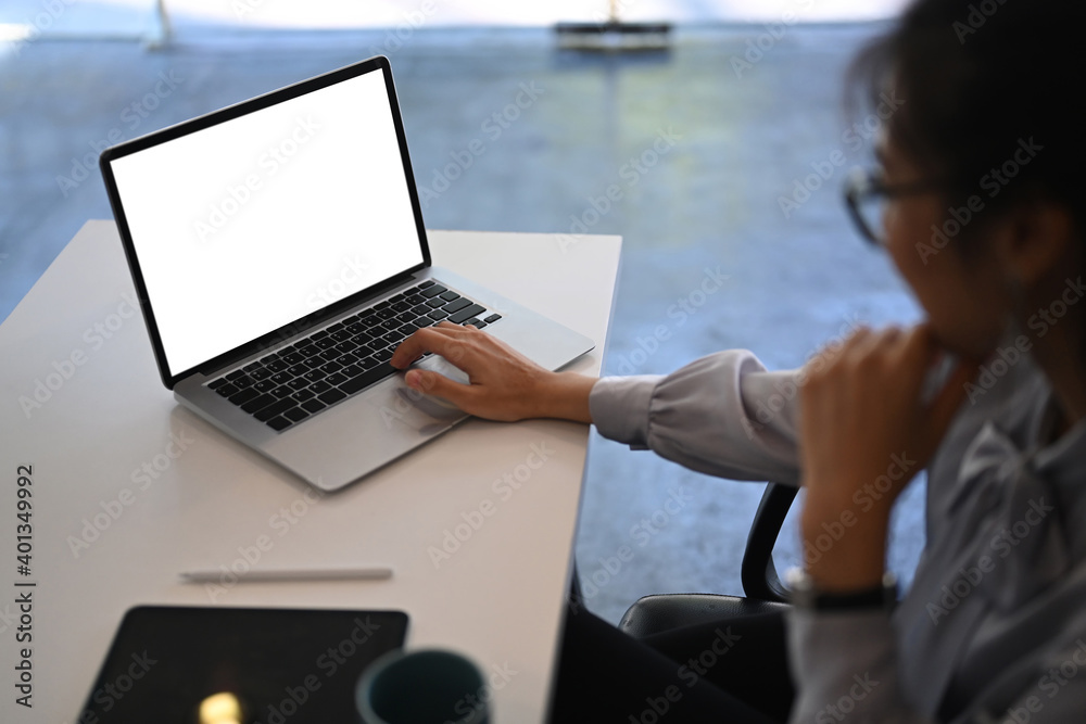 Side view of young businesswoman working on laptop computer with blank screen at office desk.