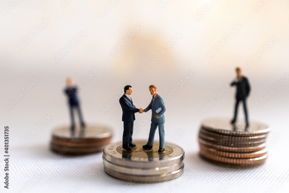 Miniature people: Businessman handshake with coins stack on world map, Investment, agreement, partnership and business concept Miniature people: Businessman handshake with coins stack on world map, Investment, agreement, partnership and business concept