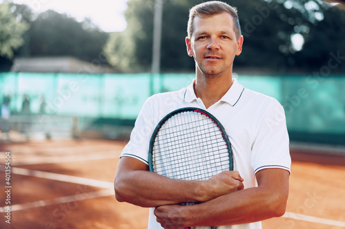 Portrait of positive male tennis player with racket standing at clay court