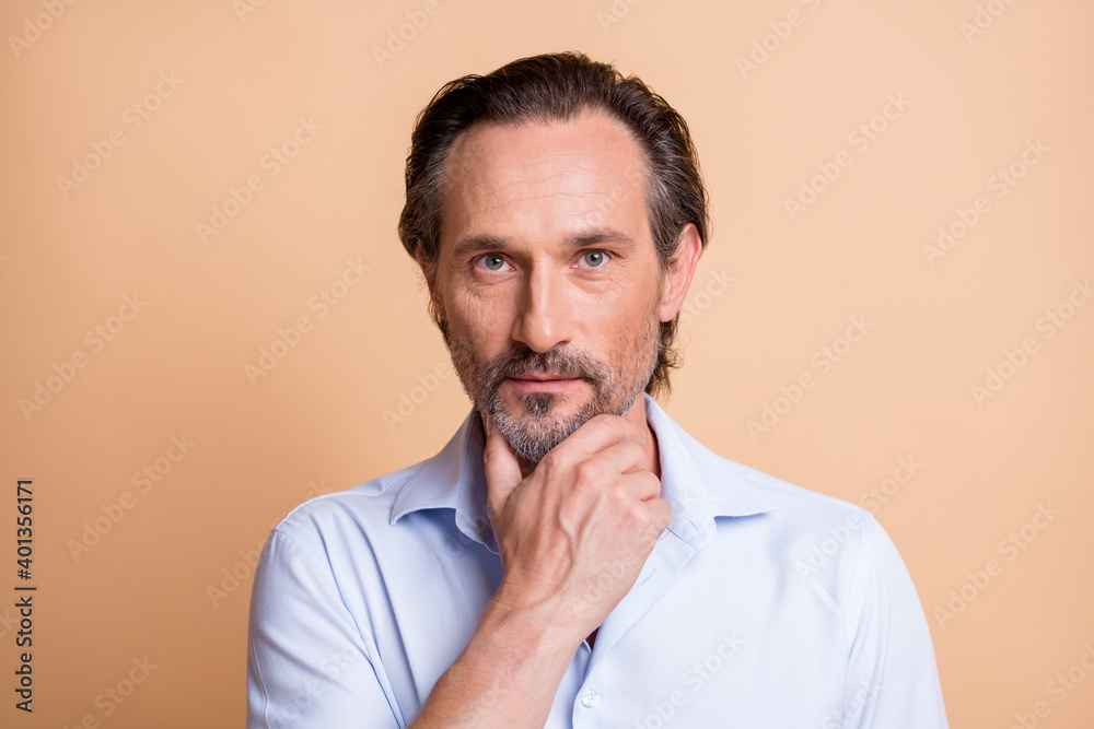 Close-up portrait of serious clever middle aged man creating strategy touching chin isolated over beige pastel color background Close-up portrait of serious clever middle aged man creating strategy touching chin isolated over beige pastel color background