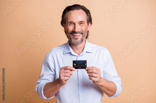 Photo of cheerful bearded man demonstrate debit card toothy smile wear shirt isolated beige color background © deagreez
