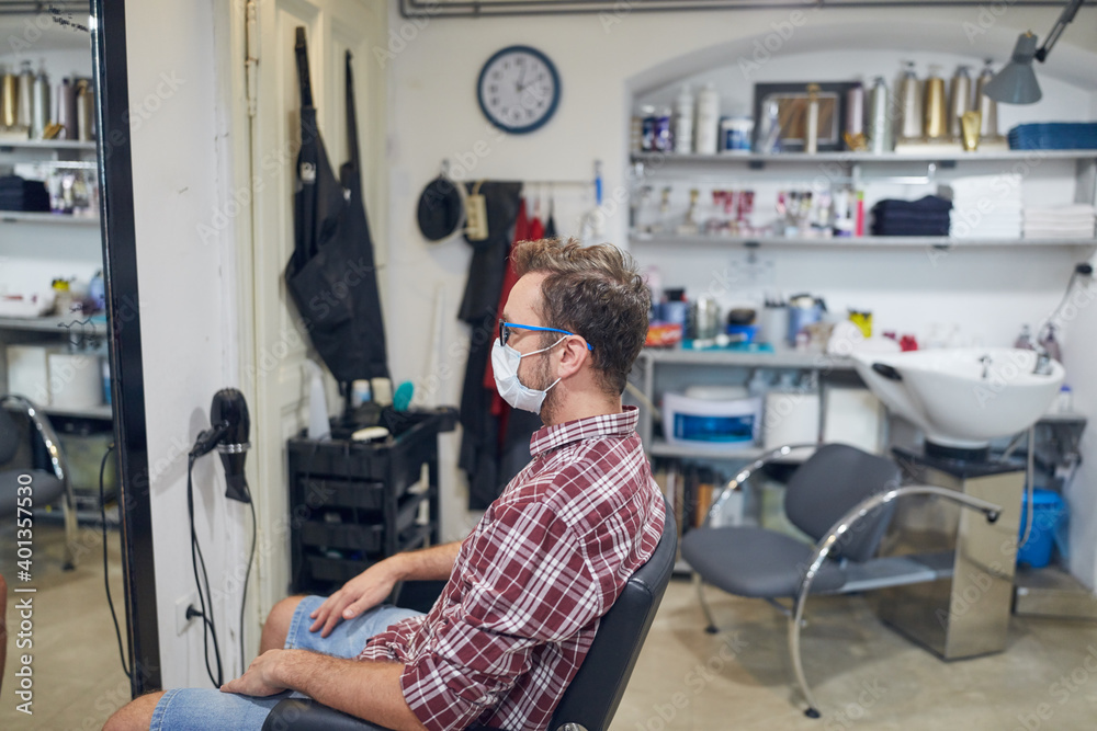 Man with surgical medical mask sitting in a hair salon. Man with surgical medical mask sitting in a hair salon.