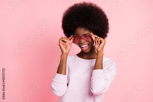 Portrait of charming flirty cheerful glad wavy-haired girl winking touching specs isolated over pink pastel color background