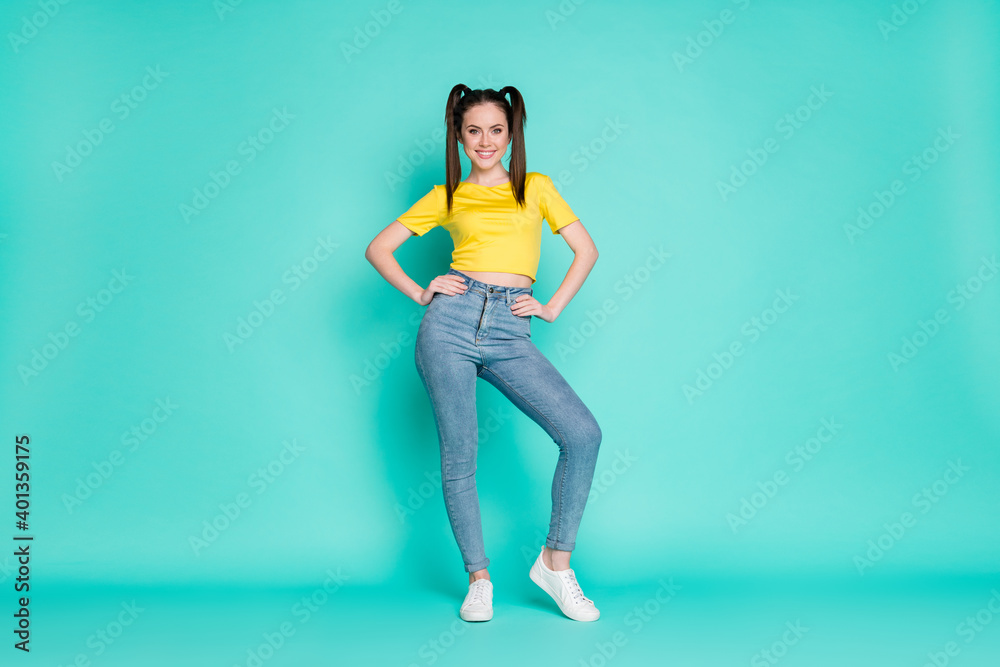 Full size photo of optimistic funky brunette girl stand wear yellow t-shirt jeans sneakers isolated on blue color background Full size photo of optimistic funky brunette girl stand wear yellow t-shirt jeans sneakers isolated on blue color background