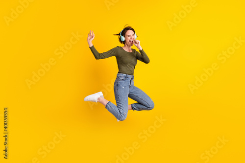 Full length photo of crazy girl jump sing song use hand as mic wear wireless headset isolated on bright yellow color background