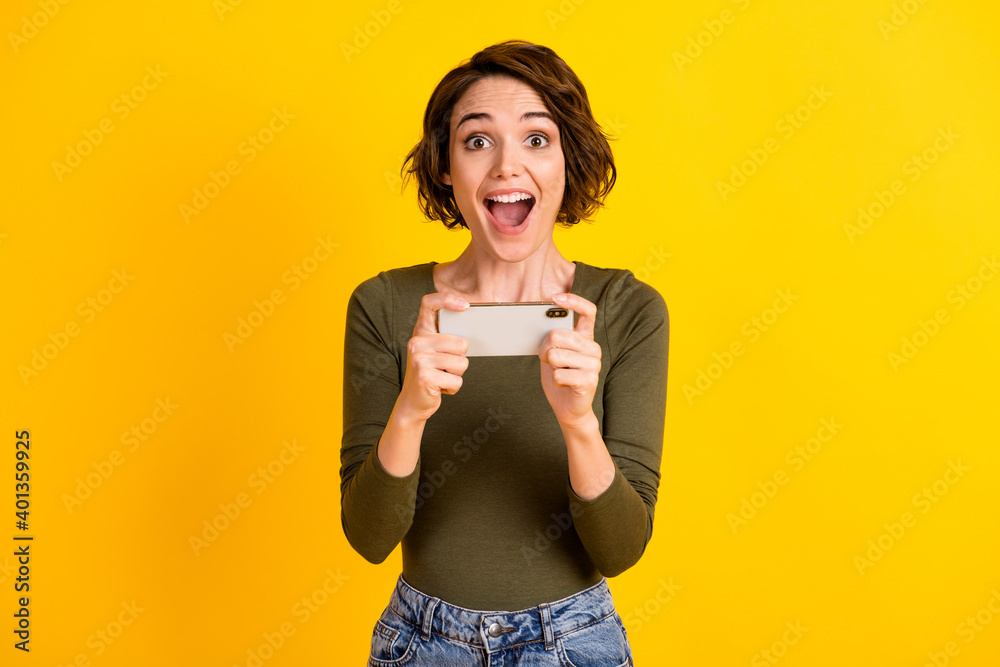 Photo of funny young lady hold telephone open mouth watch movie wear green shirt isolated vibrant yellow color background Photo of funny young lady hold telephone open mouth watch movie wear green shirt isolated vibrant yellow color background