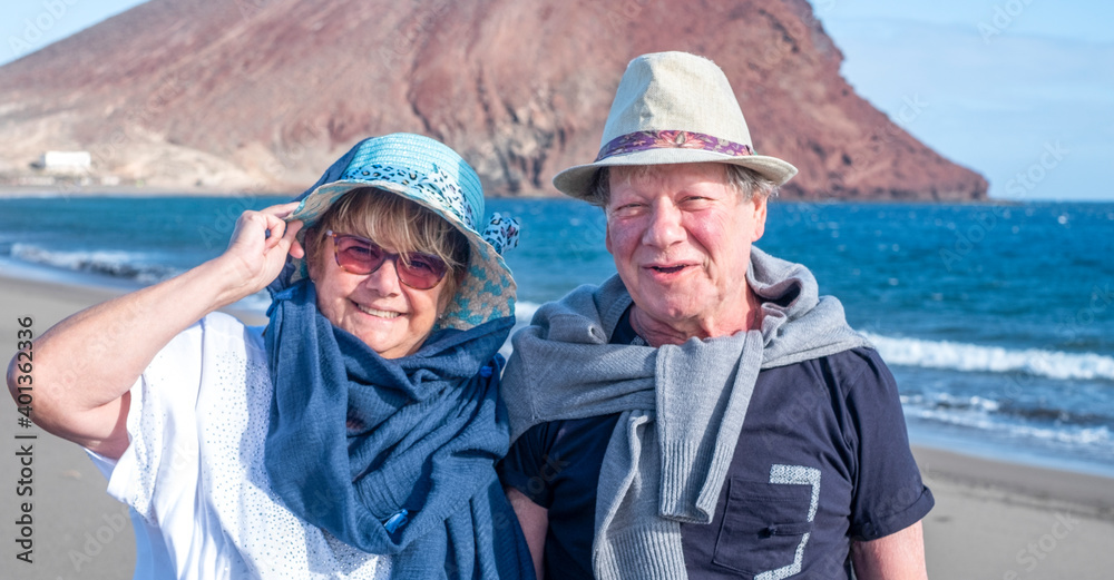 Portrait of two happy senior people enjoying winter holidays by the sea, smiling and looking at camera. Active carefree retired couple enjoying their retirement