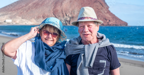 Portrait of two happy senior people enjoying winter holidays by the sea, smiling and looking at camera. Active carefree retired couple enjoying their retirement