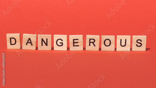 Inscription "dangerous" on wooden blocks appears on red background: warning, danger, information sign to attract attention