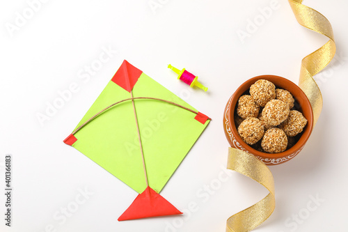 indian festival makar sankranti concept : sesame seed ball or til ke laddo and tilgul in bowl and colorful paper kite on white background