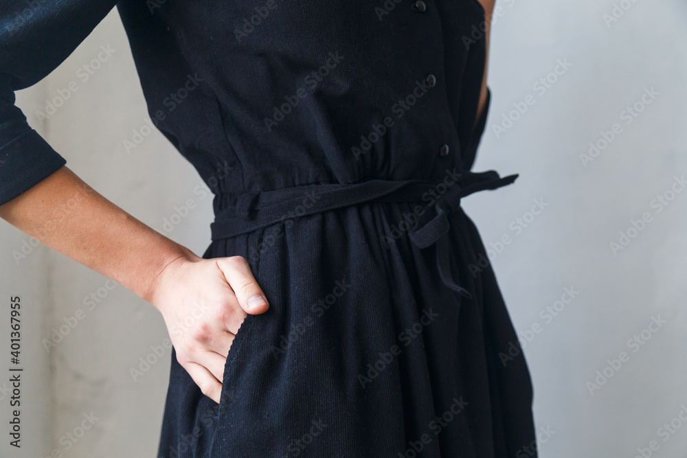 beautiful black corduroy dress on a girl close-up. Hand on the belt