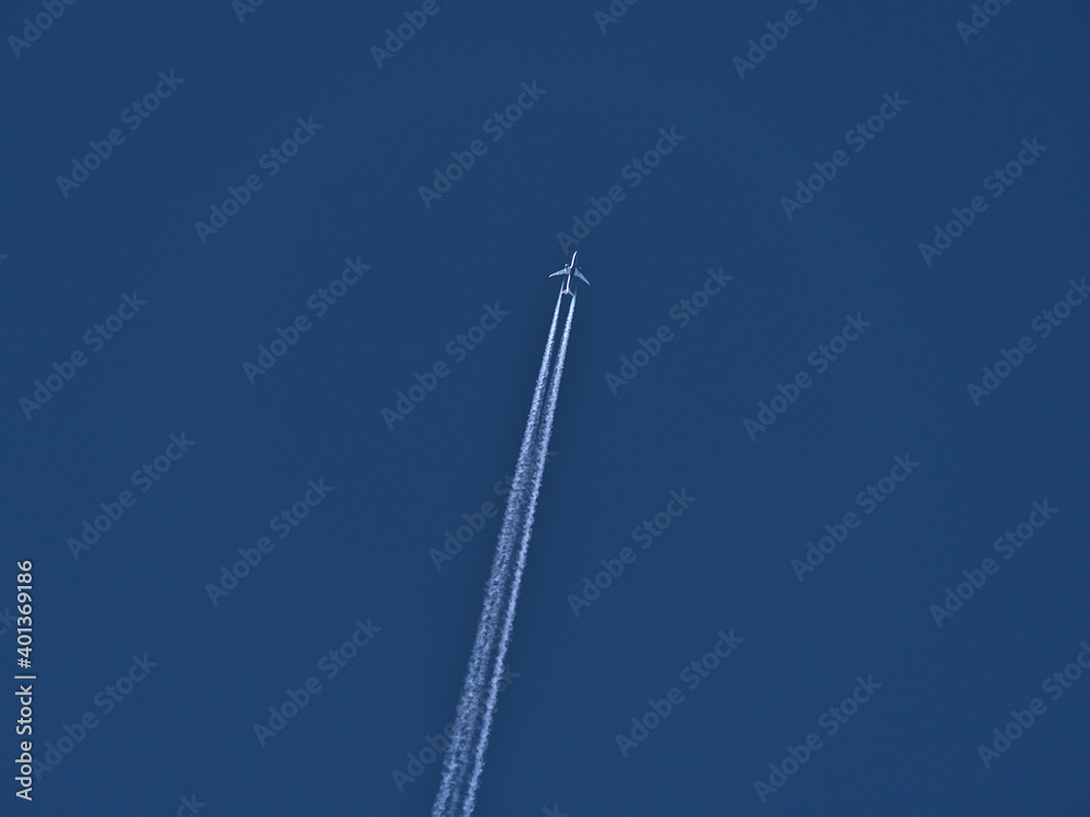 Low angle view of high flying twin-engine airplane with white colored condensation trail in clear blue sky. Low angle view of high flying twin-engine airplane with white colored condensation trail in clear blue sky.
