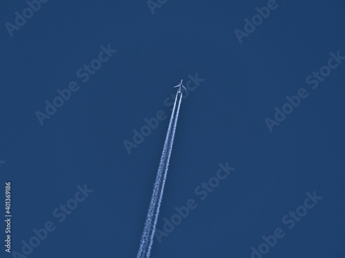 Low angle view of high flying twin-engine airplane with white colored condensation trail in clear blue sky.