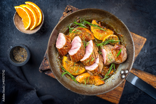 Traditional fried pork filet medaillons in with orange slices and herbs offered as top view in a rustic wrought iron skillet photo