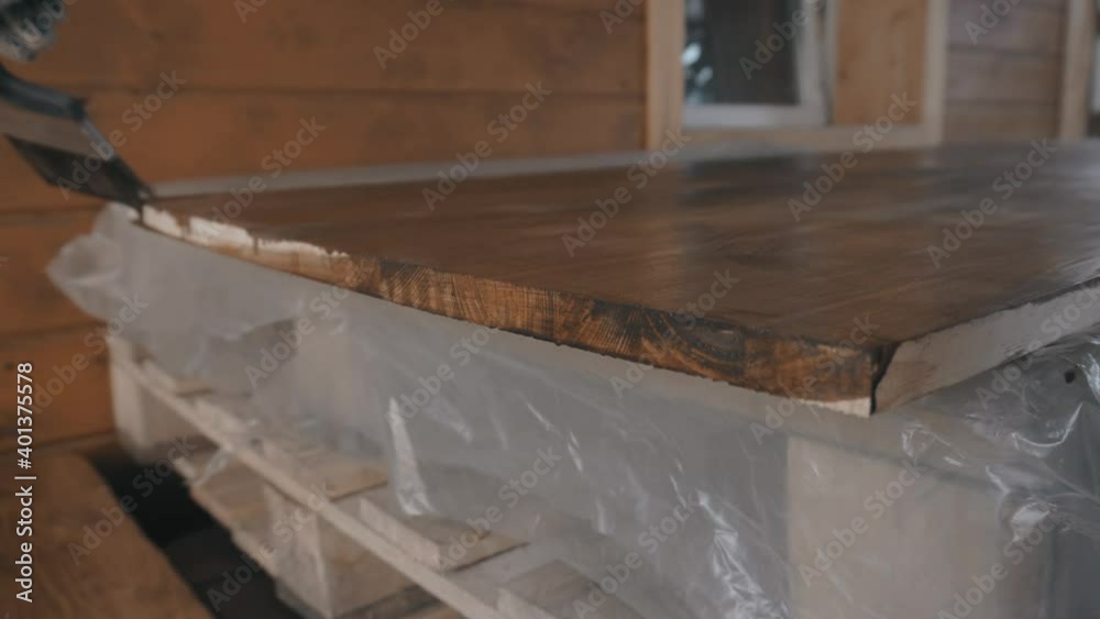 Young man in work uniform and gloves covers the ribs of a wooden tabletop Young man in work uniform and gloves covers the ribs of a wooden tabletop