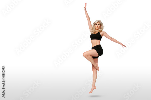 Portrait of a dancing fit young white female athlete with curly long blond hair posing by herself in a studio with a white background wearing black shorts & sports bra. © Phil