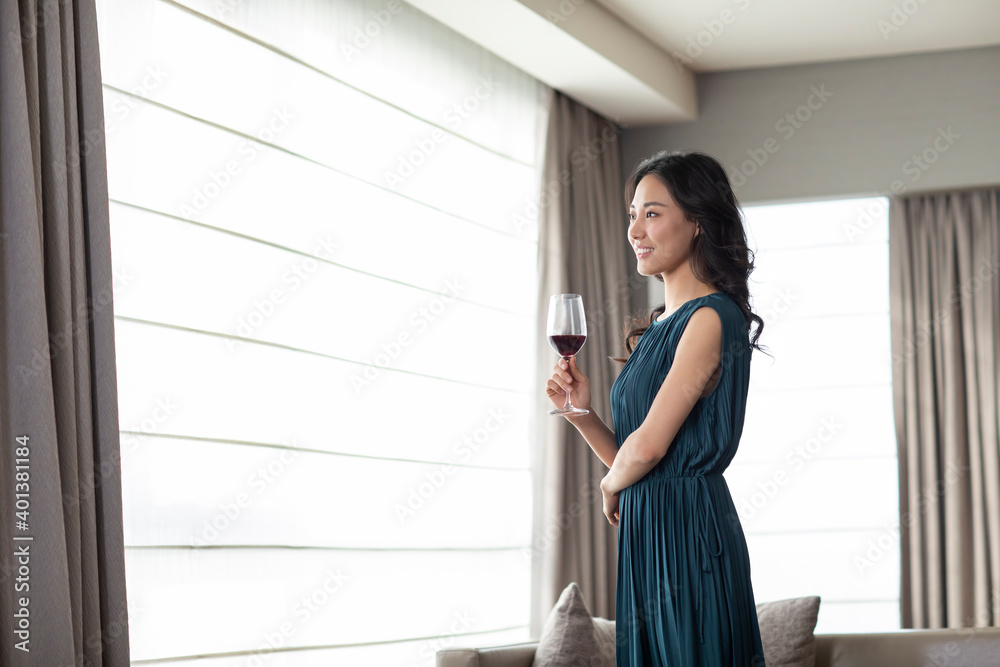 Happy young woman drinking wine in living room