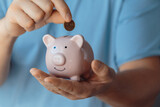 male hands puts a coin in a pink piggy bank.