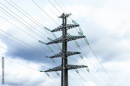 High-voltage powerful electricity tower with wires against clouds and blue sky.