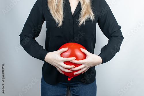 Bloating and flatulence concept. The woman holds a red balloon near the abdomen, which symbolizes bloating. Intestinal tract and digestive system. Problems with flatulence adn gastrointestinal tract