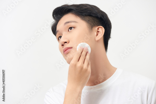 Confident young man using a cotton pad on his face isolated over a white background © makistock