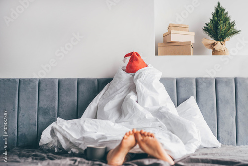  Wake up morning after party holidays. Woman in Santa hat under blanket in bed.
