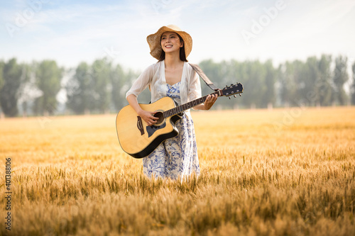 Happy young woman playing guitar in wheat field