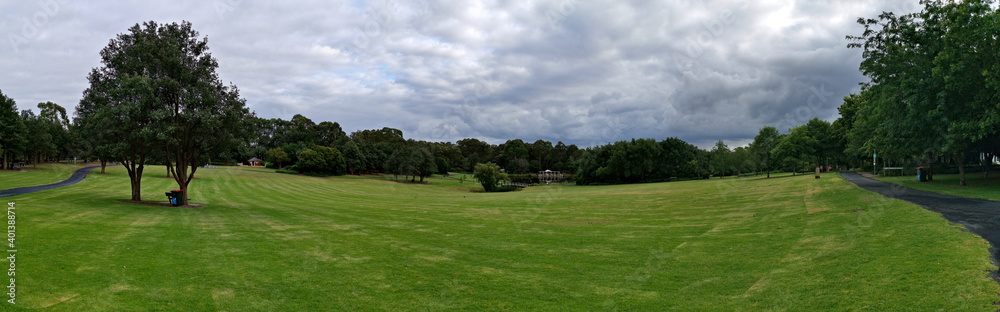Beautiful panoramic morning view of a park with green grass, tall trees and dark cloudy sky, Fagan park, Galston, Sydney, New South Wales, Australia
