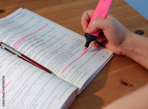 A female hand holding highlighter pen. In her workbook, she underlines important issues with a pink highlighter.