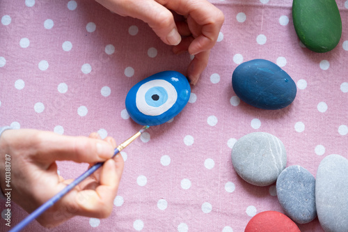 Female hands painting stone with brush.Middle aged woman's hands paint the evil eyed bead and six stone.