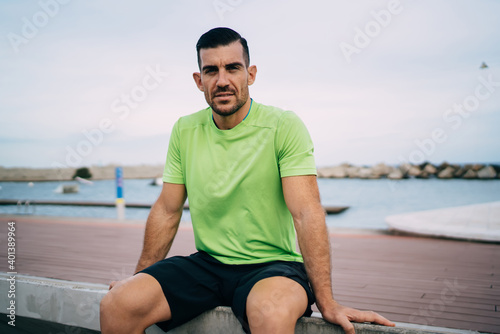 Portrait of determined sportsman 30s looking at camera during rest time at embankment, Caucasian male athletic runner in active clothing posing during training break for physical recreating