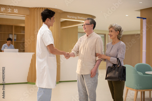 Doctor shaking hands with senior couple in hospital corridor photo