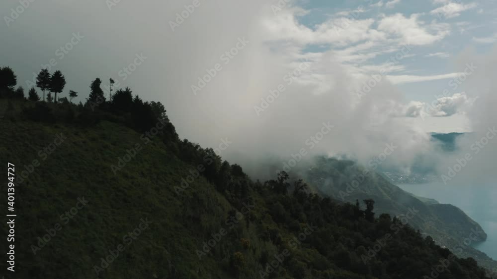 Drone aerial view rotating at the top of a mountain, the silhouette of trees next to the clouds in Lake Atitlan, Guatemala