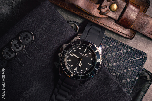 Close-up of a men's black-chrome watch on top of a sleeve with buttons and a leather bracelet