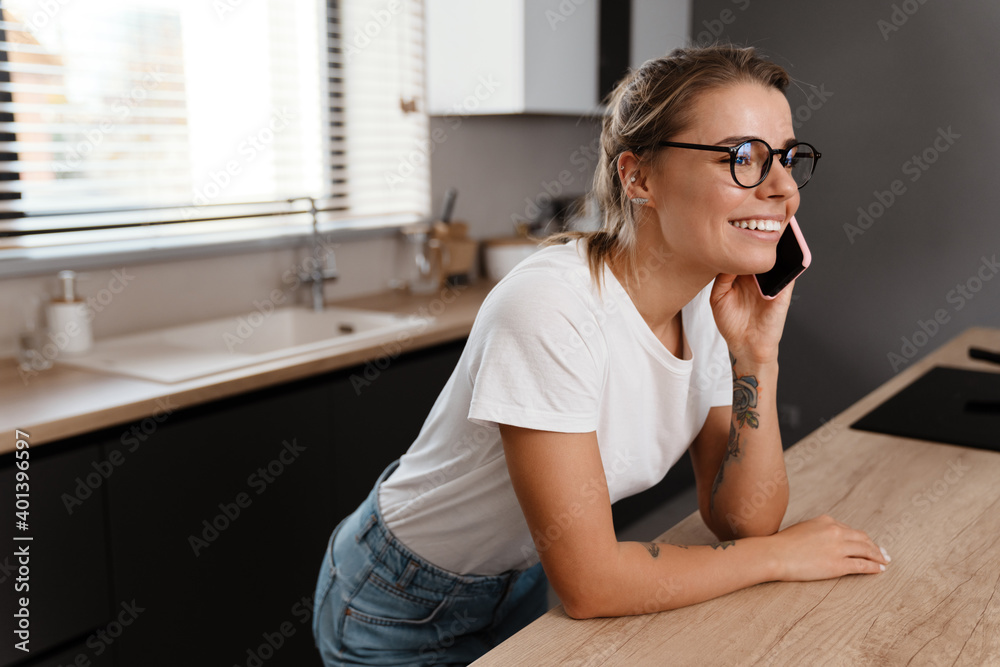 Beautiful happy girl smiling while talking on mobile phone at home kitchen Beautiful happy girl smiling while talking on mobile phone at home kitchen