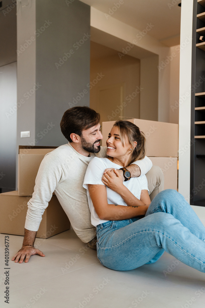 Beautiful couple hugging while sitting with boxes in new apartment Beautiful couple hugging while sitting with boxes in new apartment