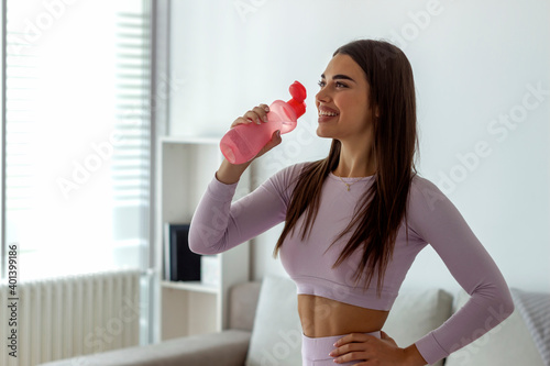 Cropped shot of a pretty young woman enjoying a bottle of water while exercising at home. Young adult girl drinking water from plastic bottle, sitting on fitness mat and resting after training at home