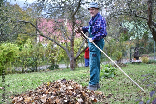 A farmer in a cottage rakes autumn leaves on a hill