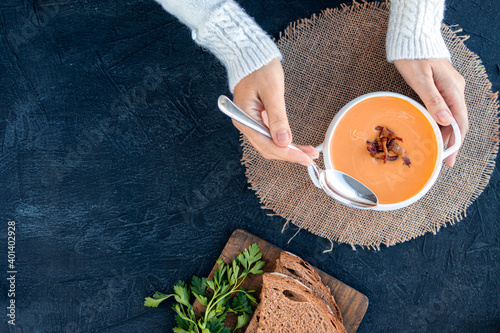 Canvas Print A woman in a white sweater eats pumpkin soup with fried bacon with bread